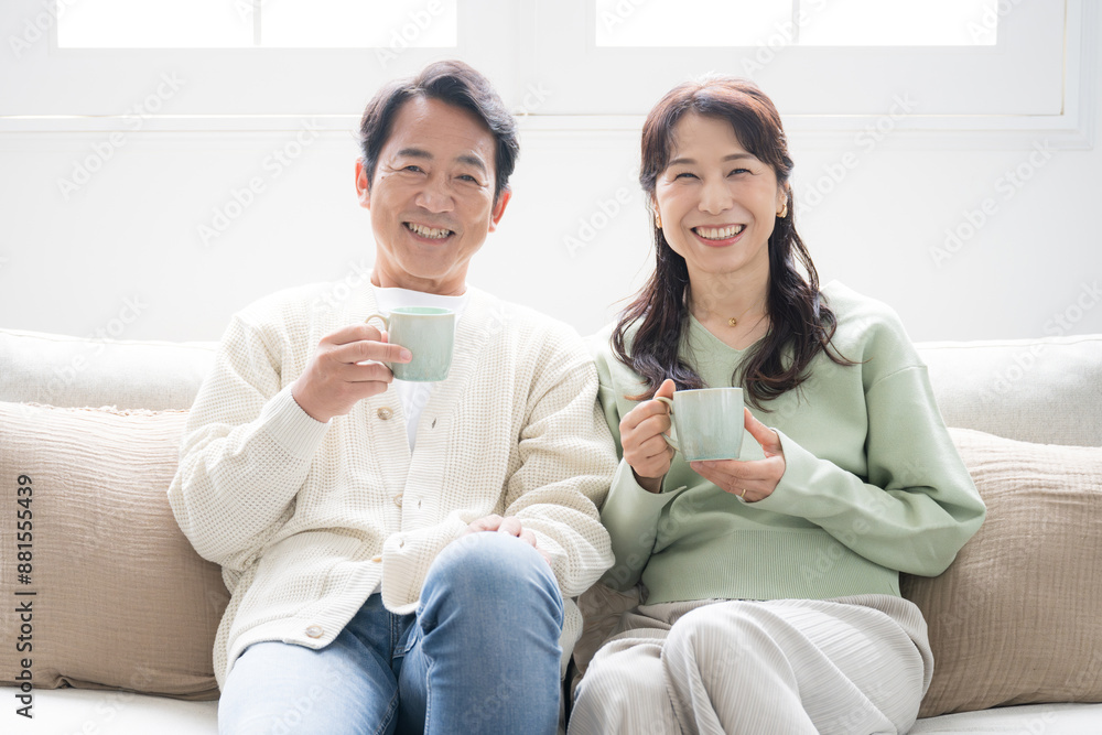 テレビや動画などを見るリビングでくつろぐ50代の夫婦の上半身 話すカップルの正面の全身 カメラ目線 テレビや動画などを見るリビングでくつろぐ50代の夫婦の上半身 話すカップルの正面の全身 カメラ目線