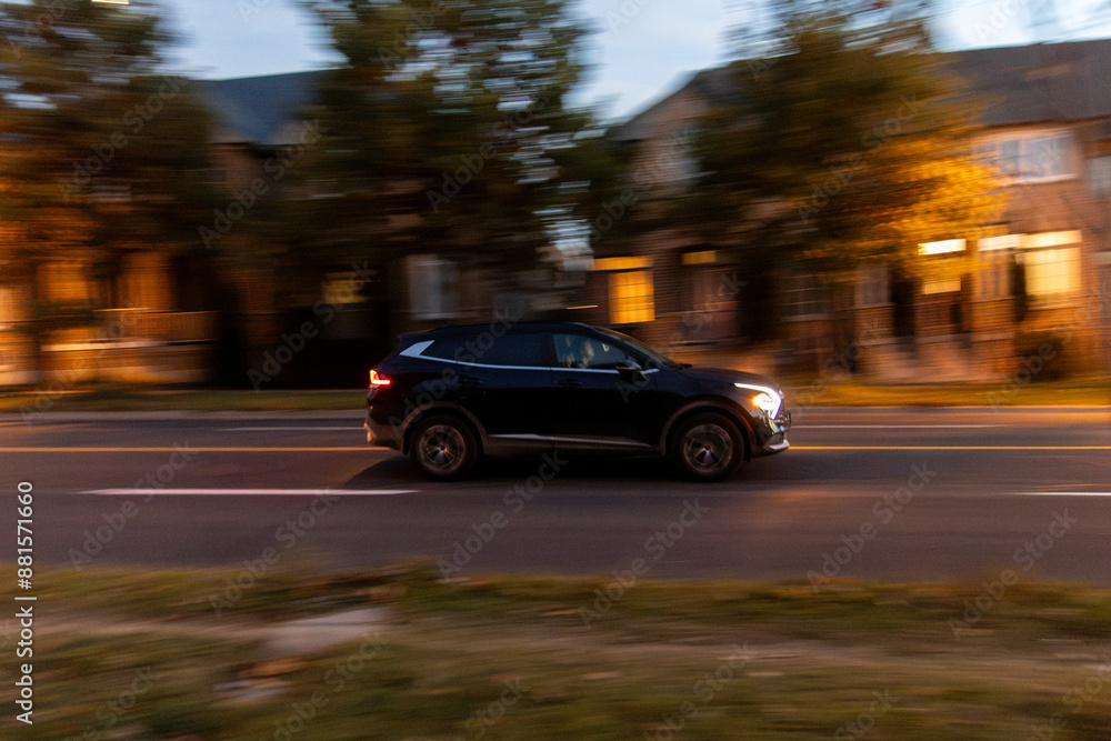 Evening urban drive - black SUV in motion blur - sunset-hued sky backdrop - residential street setting - panning photography technique. Taken in Toronto, Canada. Evening urban drive - black SUV in motion blur - sunset-hued sky backdrop - residential street setting - panning photography technique. Taken in Toronto, Canada.