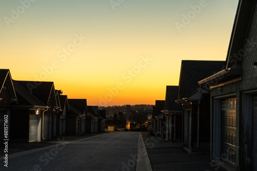 Sunset sky above suburban street - row of houses with prominent garages - warm golden hour light casting long shadows - clear, cloudless horizon - tranquil residential scene. Taken in Toronto, Canada.