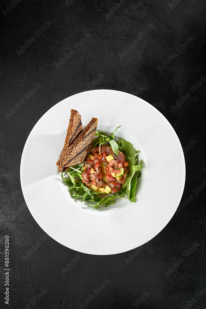 Tuna Tartare with Arugula and Toasts on White Plate - Black Background Tuna Tartare with Arugula and Toasts on White Plate - Black Background