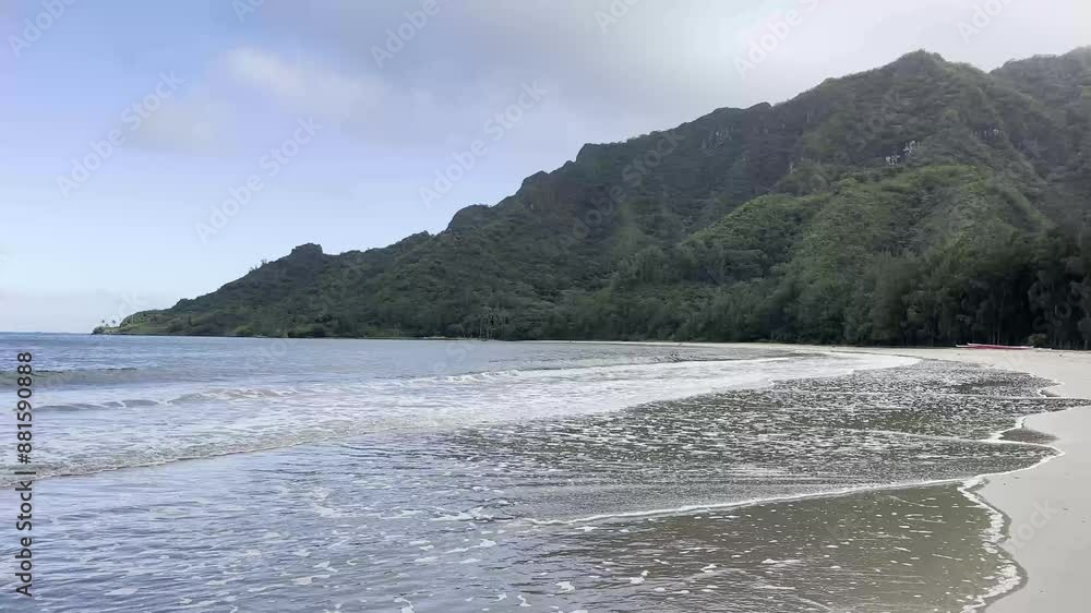 A serene beach scene with gentle waves lapping against the shore. The backdrop features lush, green mountains under a partly cloudy sky A serene beach scene with gentle waves lapping against the shore. The backdrop features lush, green mountains under a partly cloudy sky
