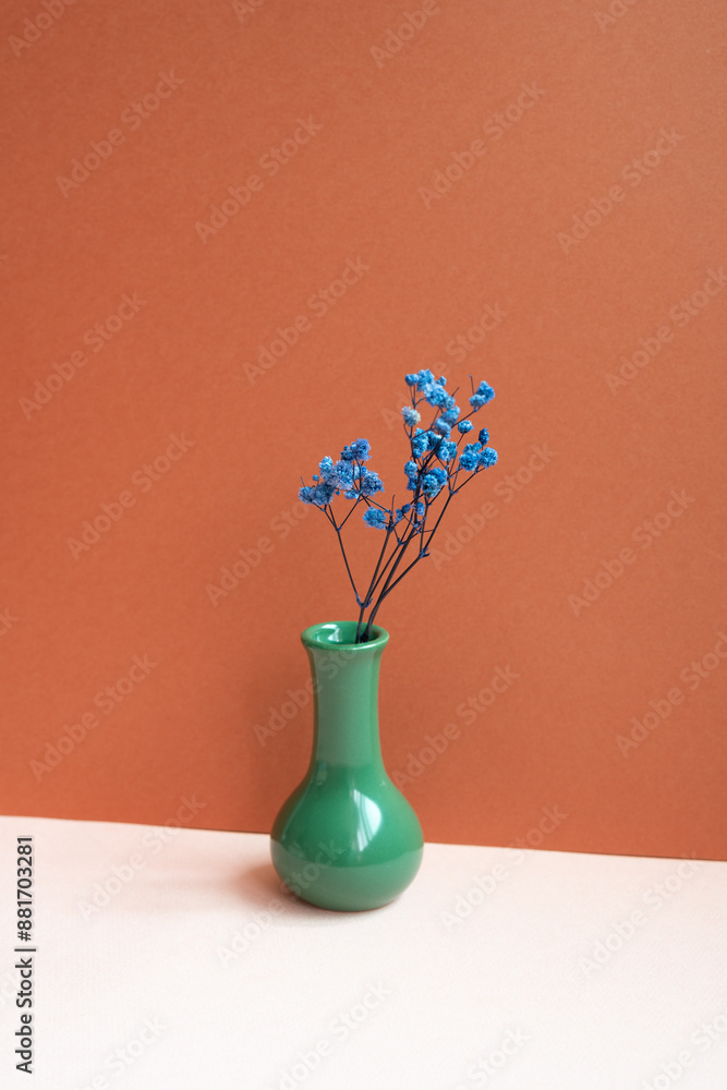 Green vase of blue dry flower on pink table. red background