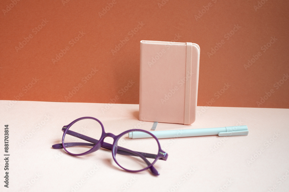 Diary notebook, pen, eyeglasses on pink desk. red background