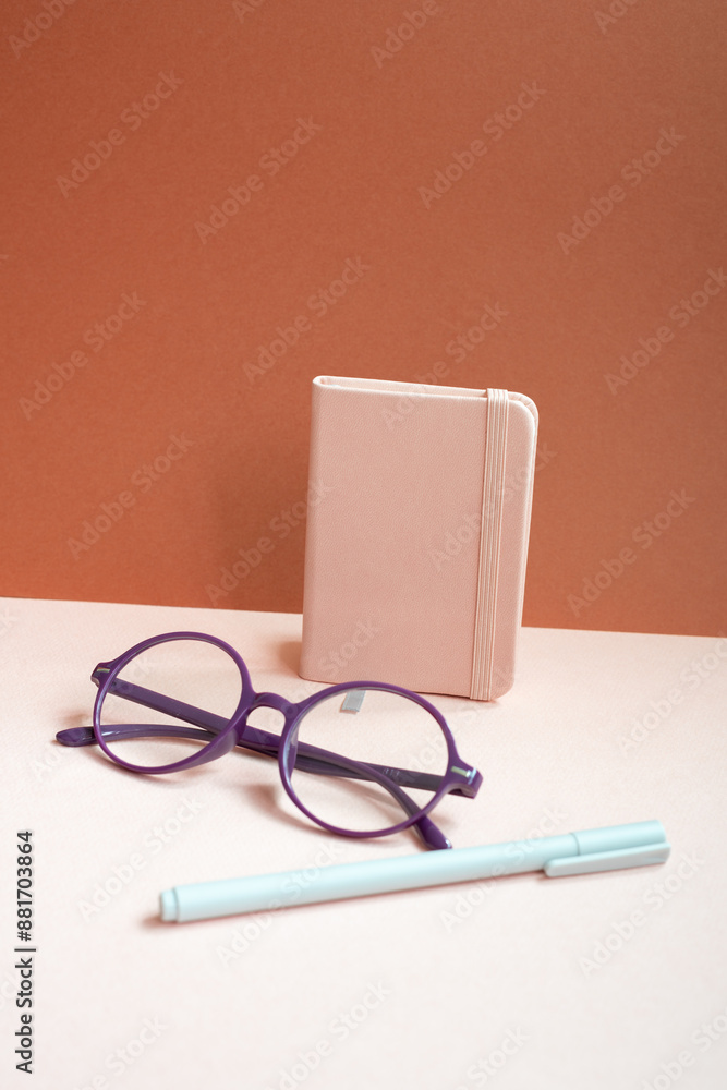 Diary notebook, pen, eyeglasses on pink desk. red background