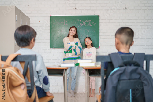 young asian female teacher introduces new schoolgirl to children in elementary school classroom