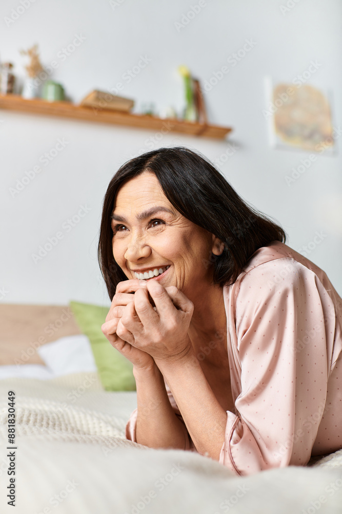 A mature woman in cozy homewear smiling on a bed.