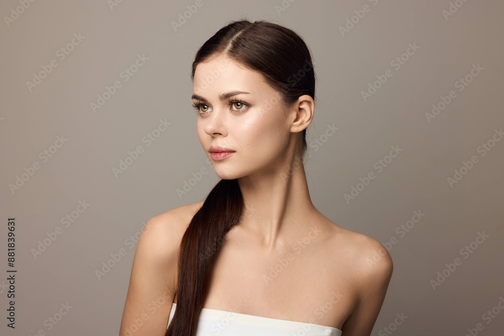 Beautiful young woman with long brown hair in a white dress looking aside against a gray background Beautiful young woman with long brown hair in a white dress looking aside against a gray background