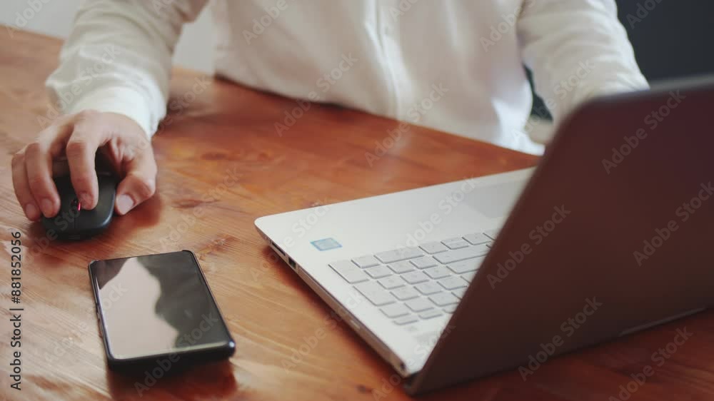 A young adult man in a white shirt works on a laptop with a wireless mouse. View from above A young adult man in a white shirt works on a laptop with a wireless mouse. View from above