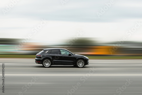 A black car is driving down the street at high speed with a blurred background. Concept of speeding, disobeying traffic rules, dangerous driving