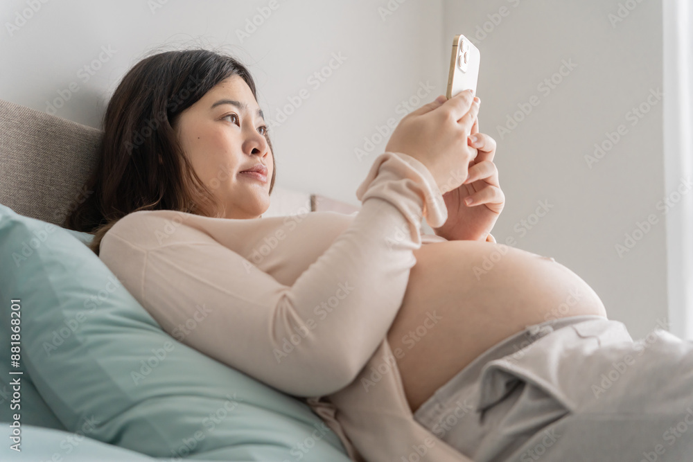 Pregnant asian woman holding smartphone at home using mobile app for pregnant women Pregnant asian woman holding smartphone at home using mobile app for pregnant women
