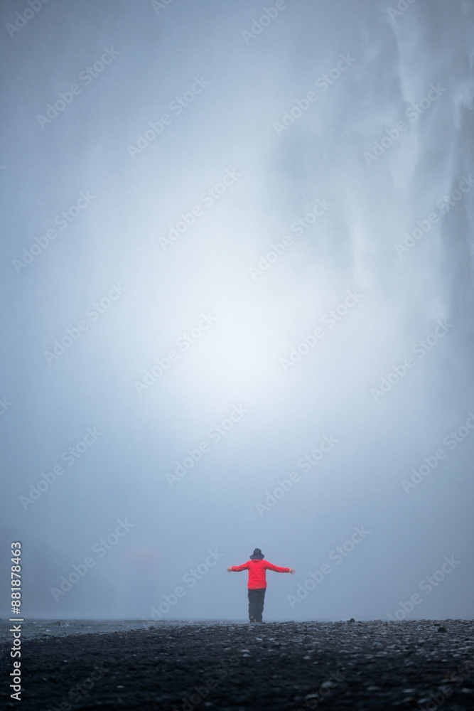 Stunning view of the Skógafoss Waterfall with a tourist wearing a red jacket. Skógafoss is one of the biggest waterfalls in Iceland, situated on the Skoga River in the south of Iceland.