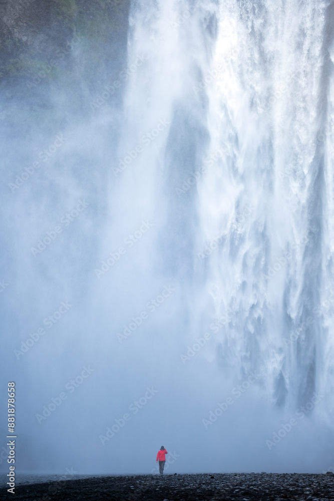 Stunning view of the Skógafoss Waterfall with a tourist wearing a red jacket. Skógafoss is one of the biggest waterfalls in Iceland, situated on the Skoga River in the south of Iceland.
