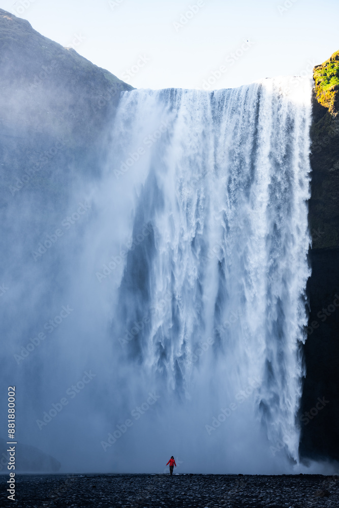 Stunning view of the Skógafoss Waterfall with a tourist wearing a red jacket. Skógafoss is one of the biggest waterfalls in Iceland, situated on the Skoga River in the south of Iceland.
