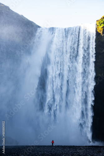 Stunning view of the Skógafoss Waterfall with a tourist wearing a red jacket. Skógafoss is one of the biggest waterfalls in Iceland, situated on the Skoga River in the south of Iceland.