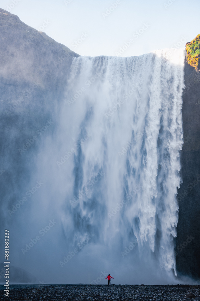 Stunning view of the Skógafoss Waterfall with a tourist wearing a red jacket. Skógafoss is one of the biggest waterfalls in Iceland, situated on the Skoga River in the south of Iceland.