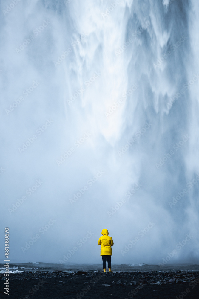 Stunning view of the Skógafoss Waterfall with a tourist wearing a yellow jacket. Skógafoss is one of the biggest waterfalls in Iceland, situated on the Skoga River in the south of Iceland.