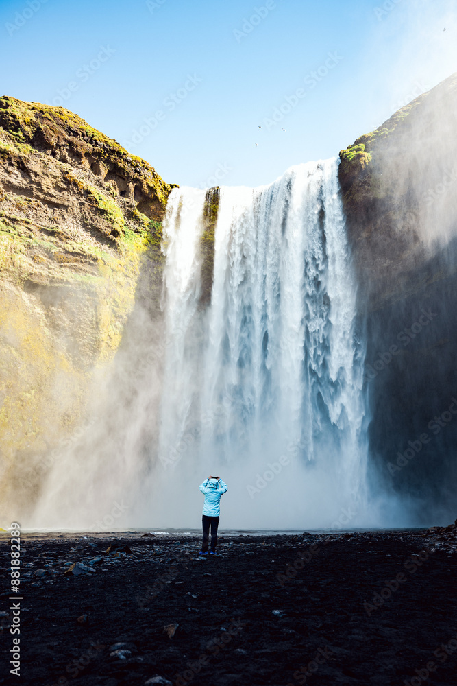 Stunning view of the Skógafoss Waterfall with a tourist taking pictures. Skógafoss is one of the biggest waterfalls in Iceland, situated on the Skoga River in the south of Iceland.
