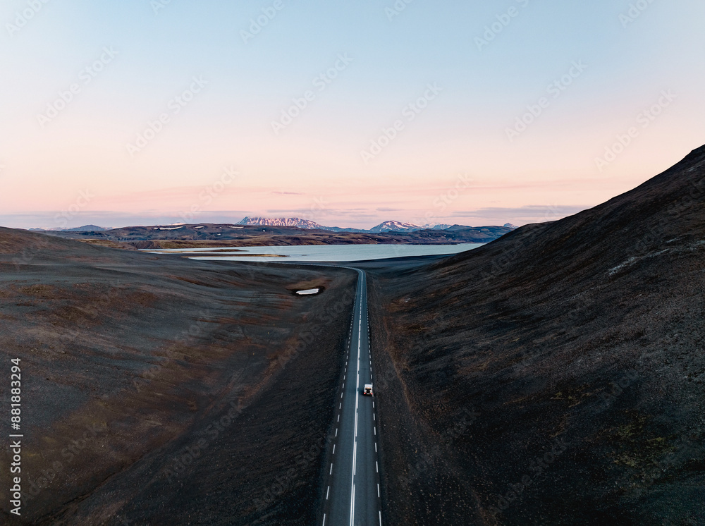 View from above, stunning aerial view of a car on a beautiful road passing through a dramatic landscape with a lake and snowy mountains in the distance, Iceland
