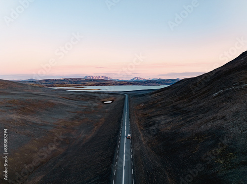 Obraz na płótnie View from above, stunning aerial view of a car on a beautiful road passing through a dramatic landscape with a lake and snowy mountains in the distance, Iceland w salonie