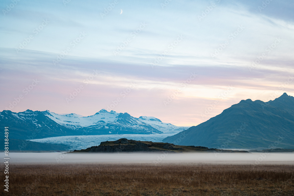 Stunning view of a dramatic landscape with some snowy mountains and a glacier in the distance during a beautiful sunrise, Iceland.