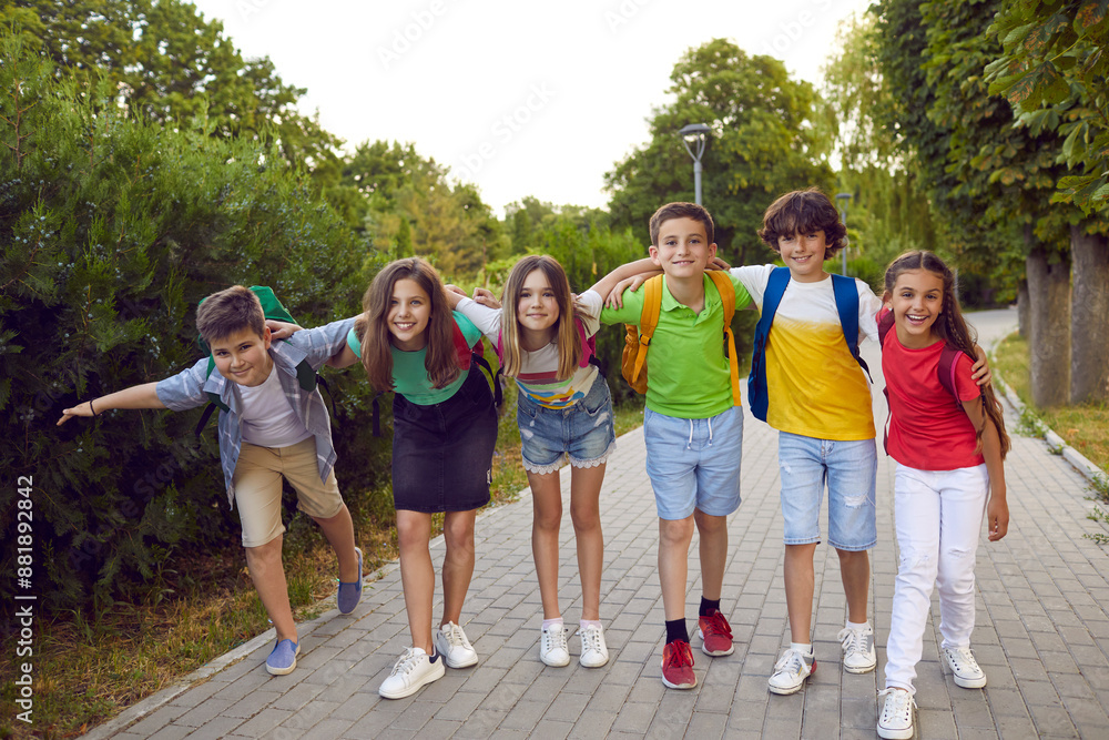 Happy school friends children boys and girls in casual clothes with backpacks standing in summer park smiling and hugging each other walking during holidays or after study day with classmates Happy school friends children boys and girls in casual clothes with backpacks standing in summer park smiling and hugging each other walking during holidays or after study day with classmates