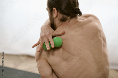 A man with a green massage ball in his right hand, doing yoga at home. photo