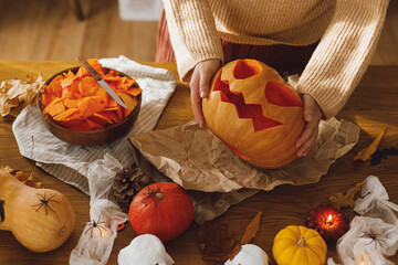 Carving halloween pumpkin. Woman holding pumpkin and knife on table with ghosts and spiders. Carve a jack o lantern, halloween preparation. Making halloween decorations