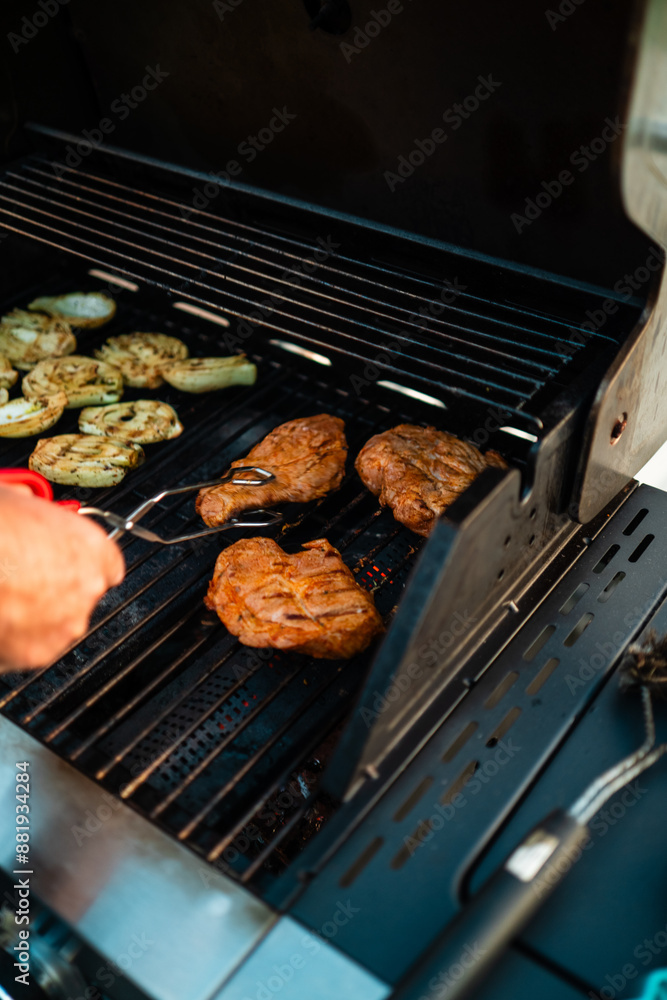 Person Grilling Steaks and Vegetables on a Big Home Gas Grill with Hot Flames During Summer Season on a Sunny Day Person Grilling Steaks and Vegetables on a Big Home Gas Grill with Hot Flames During Summer Season on a Sunny Day
