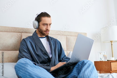 A man meditating on a bed, browsing the web on a laptop.