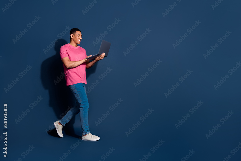 Full body length photo of young man freelancer walking using computer working remote isolated on dark blue color background Full body length photo of young man freelancer walking using computer working remote isolated on dark blue color background