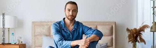 A handsome man in a bedroom, peacefully sitting on top of a bed.