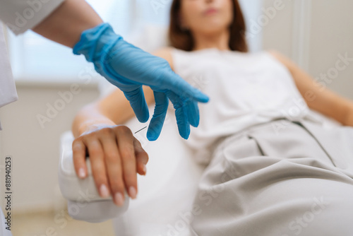 Fotografie Closeup of unrecognizable doctor acupuncturist in latex gloves inserting needle into arm of female patient during acupuncture therapy