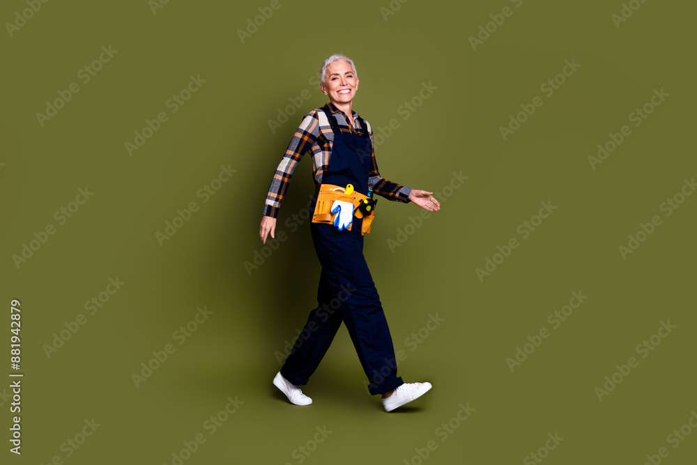 Full size photo of pretty senior female professional expert handyman walking wear blue workwear overall isolated on khaki color background Full size photo of pretty senior female professional expert handyman walking wear blue workwear overall isolated on khaki color background