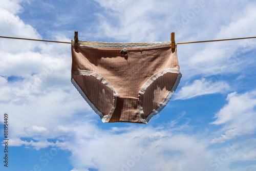 Obraz na płótnie women's panties hang and dry on a clothesline on wooden clothespins and flutter in the wind against the blue sky with cloudscape w salonie