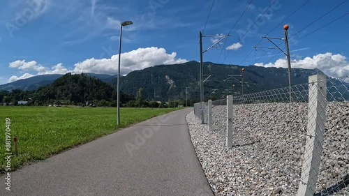 Fahrradweg entlang einer Eisenbahnlinie in der Ferne Berge und blauer Himmel mit Wolken