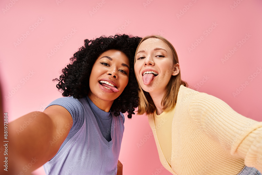 Two women in casual attire taking a selfie in front of a pink wall. Two women in casual attire taking a selfie in front of a pink wall.