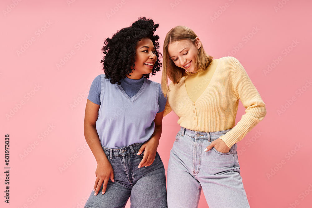 Two diverse women stand stylishly in front of a pink backdrop. Two diverse women stand stylishly in front of a pink backdrop.
