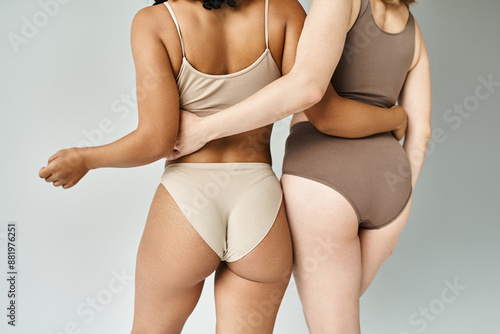 Two beautiful diverse women in cozy pastel underwear standing side by side.