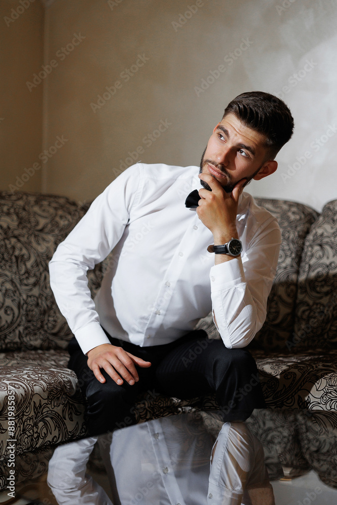 Obraz premium A man in a white shirt and black pants is sitting on a couch, looking at the camera