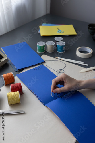 High-quality image of a person binding a book using traditional coptic stitch technique. DIY bookbinding, handcrafting, artisan book, handmade, coptic stitch, binding tools, creative, detailed process photo