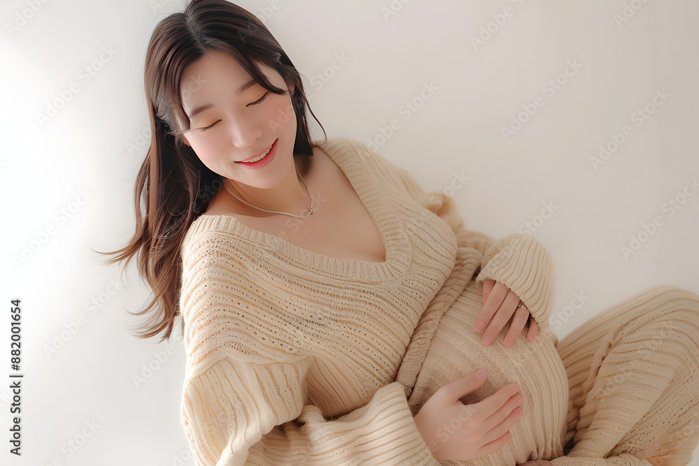 Beautiful Asian Pregnancy happiness woman smile in knit shirt touch belly waiting for unborn baby on beige isolated background. Mom holding tummy. Journey to motherhood. Beautiful Asian Pregnancy happiness woman smile in knit shirt touch belly waiting for unborn baby on beige isolated background. Mom holding tummy. Journey to motherhood.