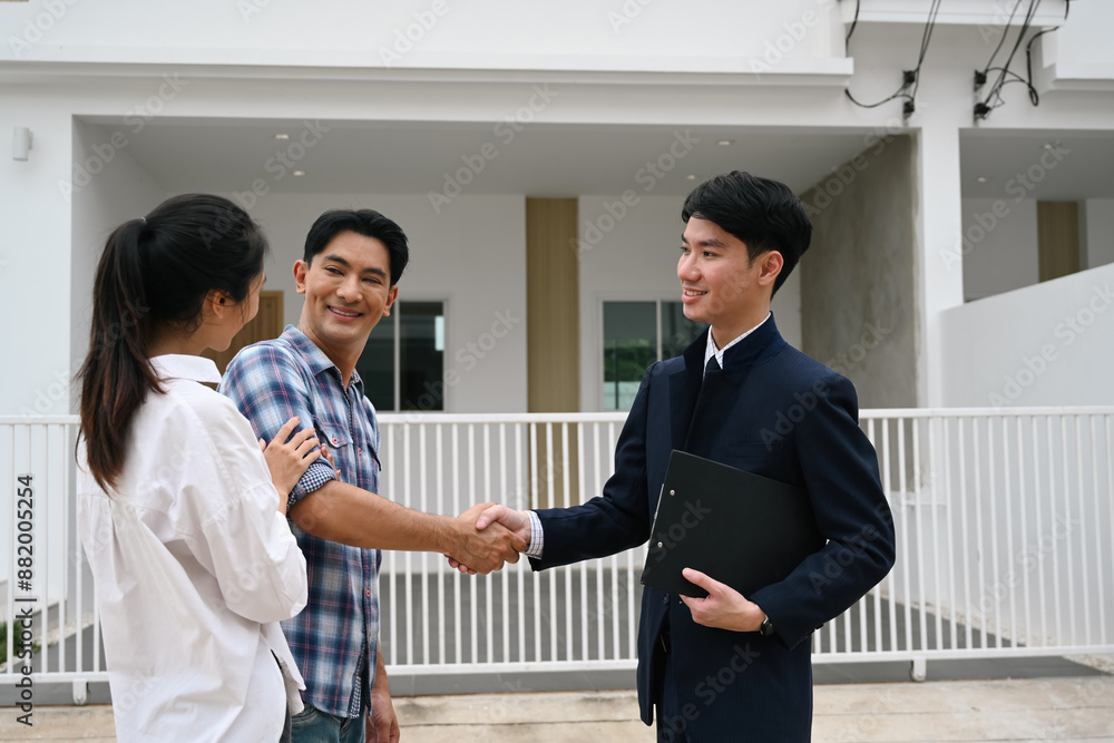 Welcome Home and A New Beginning, A couple smiles and shakes hands with a real estate agent in front of a newly completed home Welcome Home and A New Beginning, A couple smiles and shakes hands with a real estate agent in front of a newly completed home