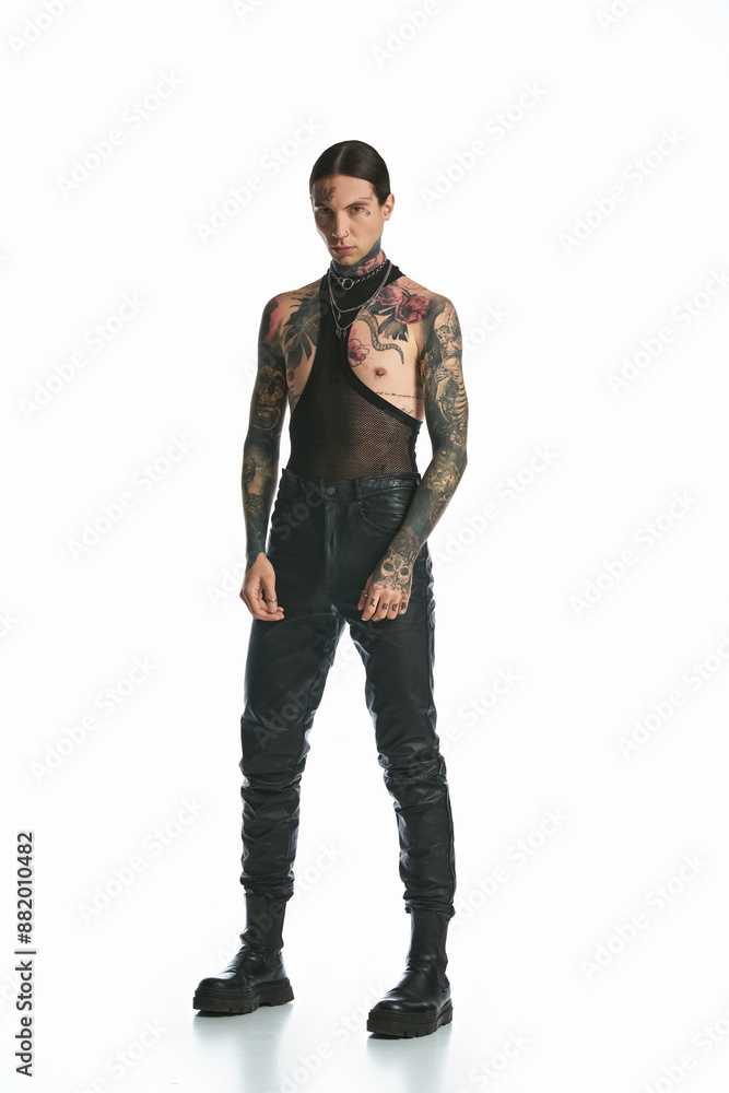 A young man with tattoos poses confidently in front of a white background. A young man with tattoos poses confidently in front of a white background.