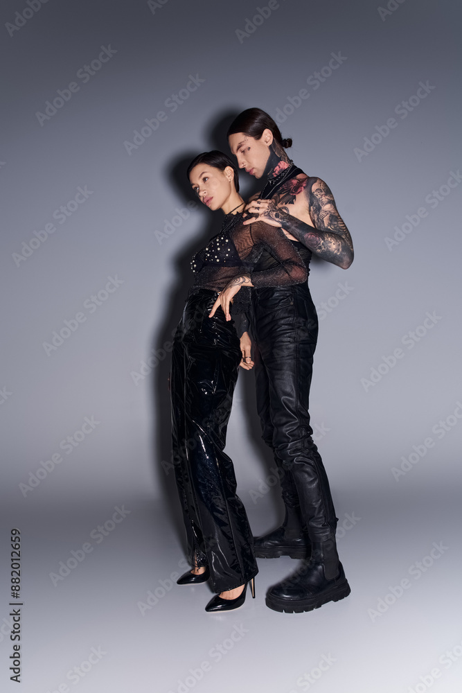A young tattooed couple posing gracefully in a studio against a grey background.