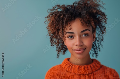 Woman With Curly Hair Smiling In An Orange Sweater Against A Blue Background