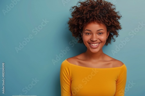 Smiling Woman With Curly Hair Wearing Yellow Shirt Against Blue Background