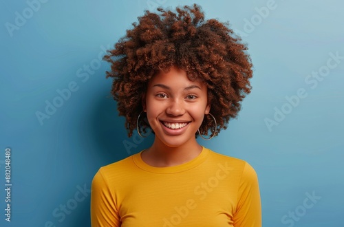 Smiling Woman With Curly Hair Wearing Yellow Shirt Against Blue Background