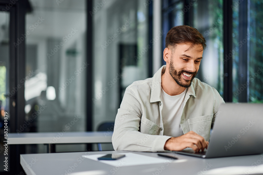A smiling man working over the laptop, at the co-working space. A smiling man working over the laptop, at the co-working space.