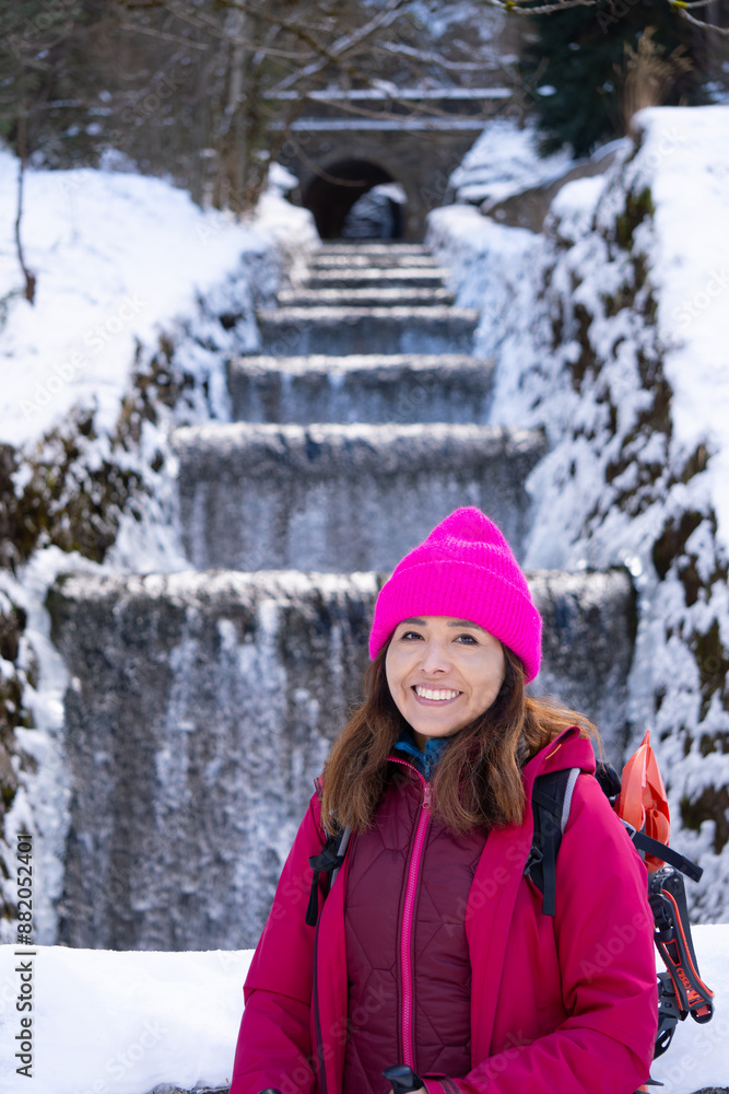 happy young adventure tourism mountaineer woman with shiver looks at camera, behind frozen snow covered winter waterfall and stone bridge. Concept: Winter sports and tourism. Canfranc Pyrenees. happy young adventure tourism mountaineer woman with shiver looks at camera, behind frozen snow covered winter waterfall and stone bridge. Concept: Winter sports and tourism. Canfranc Pyrenees.