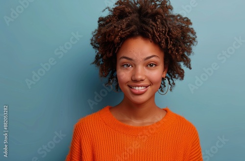 Woman With Curly Hair Smiling In An Orange Sweater Against A Blue Background